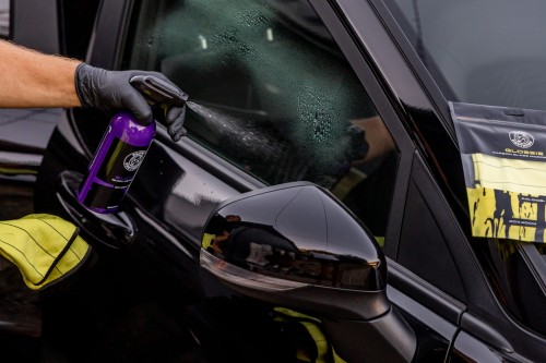 Prezentacja butelki BLOOM Quick Detailer na tle samochodu w profesjonalnym warsztacie