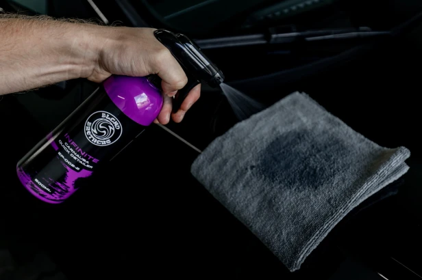Prezentacja INFINITE Carnauba Quick Detailer przy masce samochodu podczas pielęgnacji.
