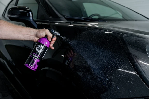 Zbliżenie na butelkę INFINITE Carnauba Quick Detailer trzymaną przy karoserii auta