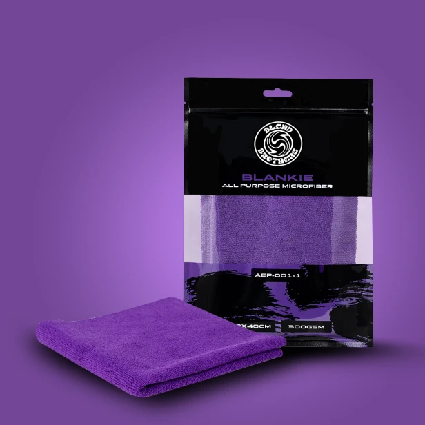 Fioletowa mikrofibra uniwersalna Blankie 300GSM obok czarnego opakowania strunowego Blend Brothers na fioletowym tle.