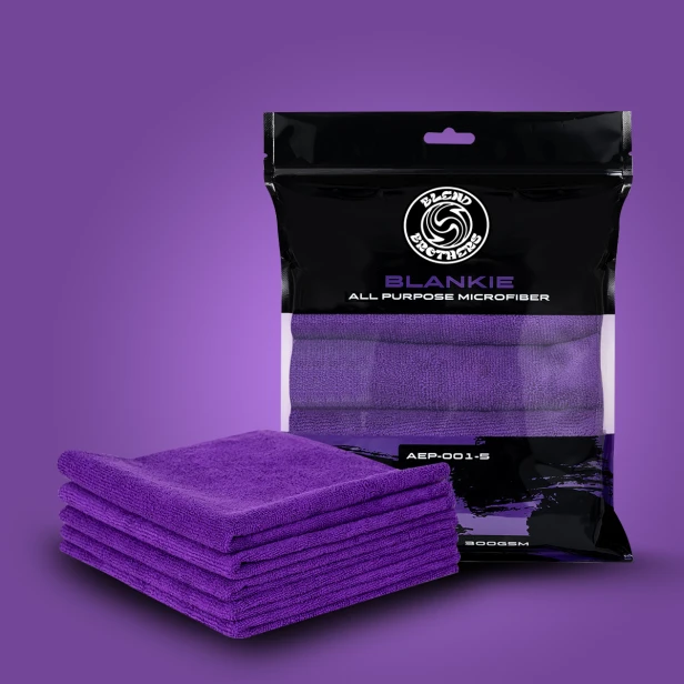 Zestaw 5 fioletowych mikrofibr Blankie w czarnym opakowaniu zbiorczym obok stosu 5 sztuk na fioletowym tle.