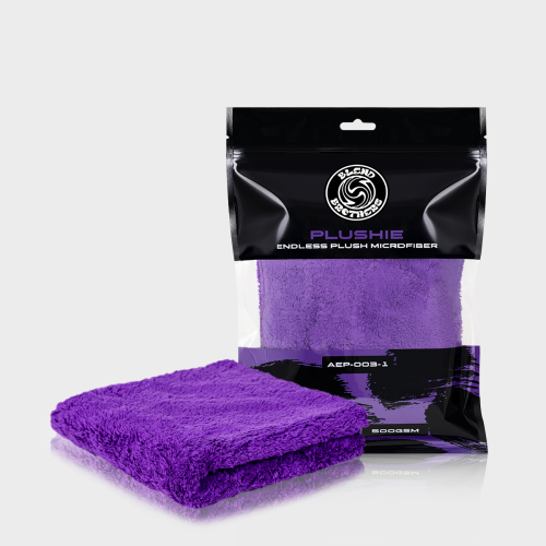 Packshot fioletowej mikrofibry Plushie 1 sztuka wraz z opakowaniem na jasnym tle z odbiciem.