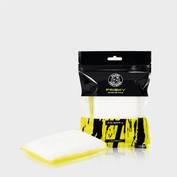 Dwustronny pad czyszczący Frisky Scrub Pad obok czarnego opakowania na limonkowym tle.