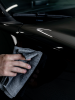 Zbliżenie na butelkę INFINITE Carnauba Quick Detailer trzymaną przy karoserii auta.