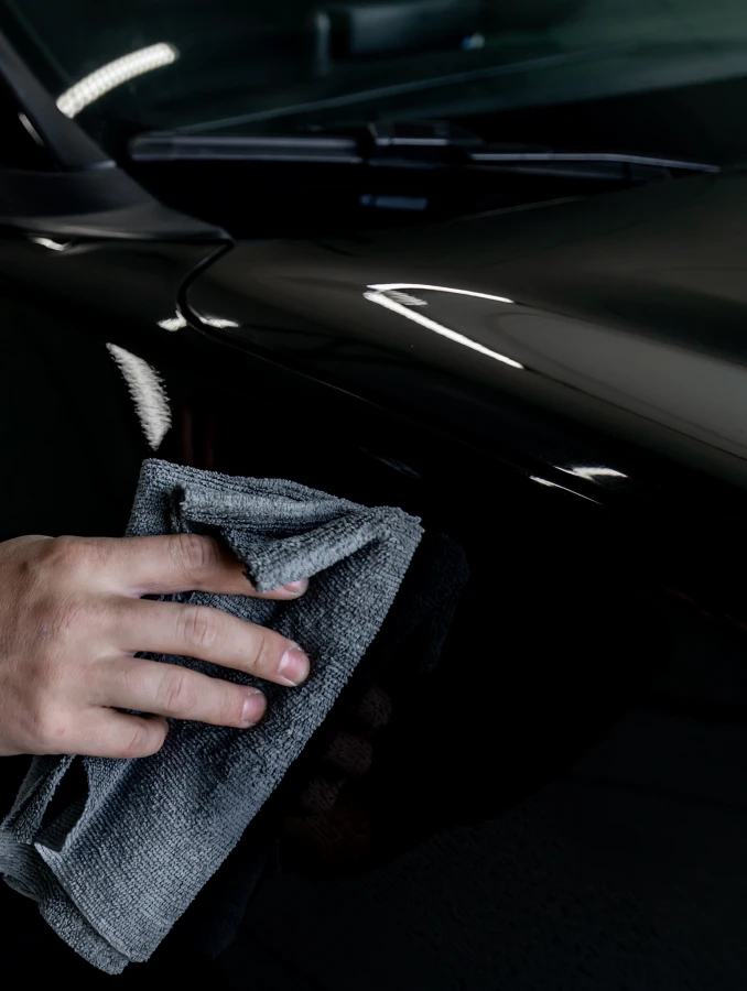 Zbliżenie na butelkę INFINITE Carnauba Quick Detailer trzymaną przy karoserii auta.