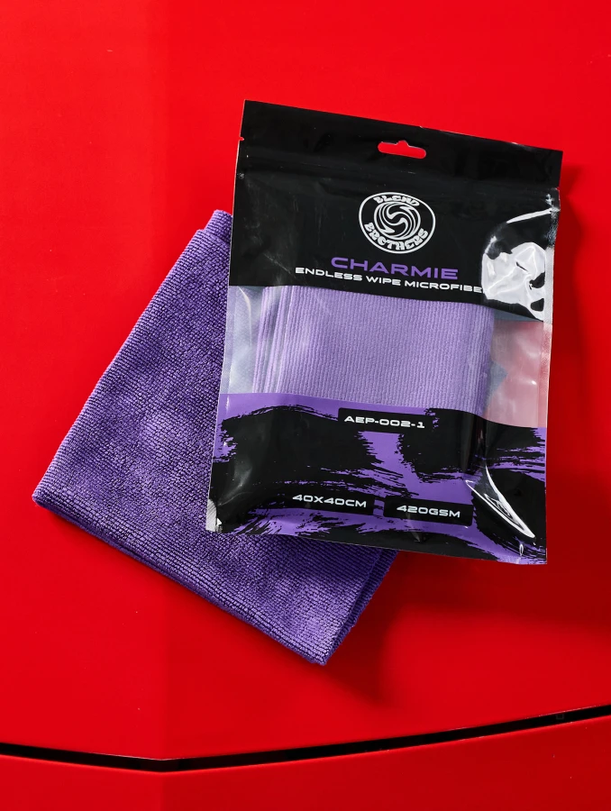 Fioletowa mikrofibra Blend Brothers Charmie 1 sztuka do zabezpieczania lakieru i powierzchni zewnętrznych. Pokazanie mikrofibry z opakowanie i bez na czerwonym lakierze.